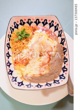 Traditional Mexican cheese enchiladas served with rice and refried beans on decorative plate 137308485