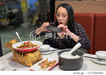 Happy Asian Woman Photographing Spicy Chinese Dish with Smartphone in Restaurant 137308490
