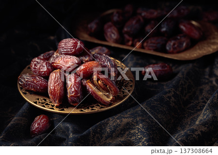 Dates fruits in a golden bowl on black fabric with gold ornamentation. Dates fruits in a golden bowl on black fabric with gold ornamentation. 137308664