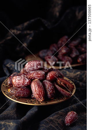 Dates fruits in a golden bowl on black fabric with gold ornamentation. 137308665