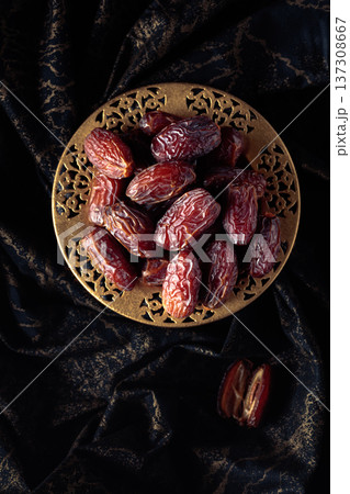 Dates fruits in a golden bowl on black fabric with gold ornamentation. 137308667