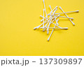 Cotton swabs, also known as q-tips or ear sticks, scattered on a bright yellow background representing personal hygiene and medical care 137309897