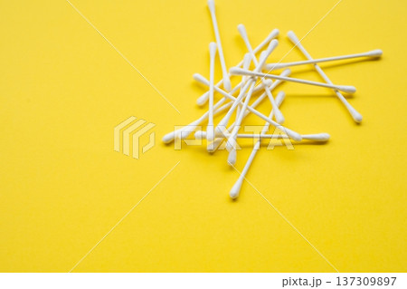 Cotton swabs, also known as q-tips or ear sticks, scattered on a bright yellow background representing personal hygiene and medical care 137309897