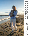 Woman holding a puppy, walking on a sandy beach as the sun sets, enjoying pet ownership and peaceful leisure time 137309903