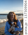 A young woman hugs her Cavalier King Charles Spaniel on the beach at sunset. Warm light, waves, and smiles capture a peaceful, joyful moment of connection and relaxation. 137309904