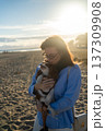 Woman holding and kissing her small pet dog, a cavalier king charles spaniel, enjoying a bond on the beach 137309908