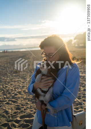 Woman holding and kissing her small pet dog, a cavalier king charles spaniel, enjoying a bond on the beach 137309908