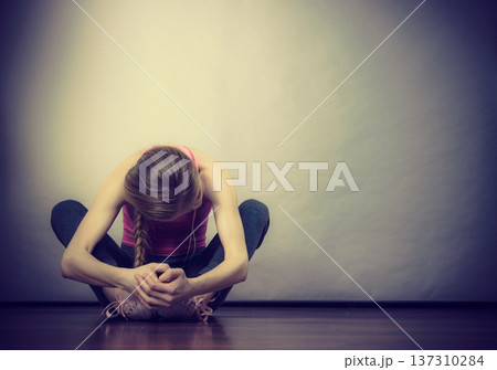 Sad depressed young teenage girl sitting by wall 137310284