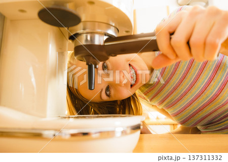 Woman in kitchen making coffee from machine 137311332