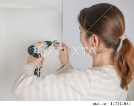 A Caucasian woman uses a screwdriver to tighten a screw while assembling a cabinet. 137311683
