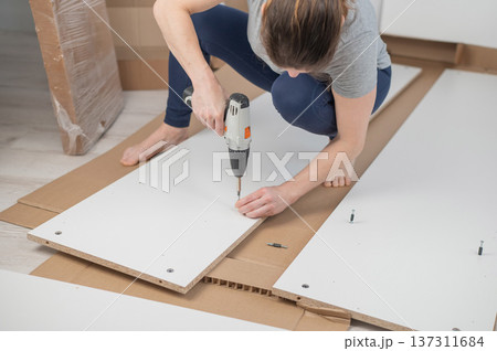 A Caucasian woman uses a screwdriver to tighten a screw while assembling a cabinet. 137311684