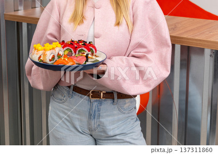 A woman holds a plate of assorted sushi rolls 137311860
