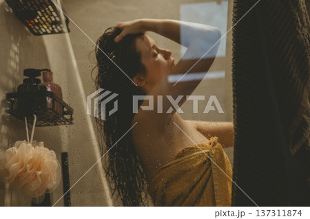 Young woman practicing self-care ritual in cozy bathroom, washing hair behind glass shower door with water drops, cinematic warm lighting, mental health and morning routine concept authentic lifestyle Young woman practicing self-care ritual in cozy bathroom, washing hair behind glass shower door with water drops, cinematic warm lighting, mental health and morning routine concept authentic lifestyle 137311874