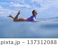 Youthful Female Surfer Smiling Peacefully On Her Board With Tropical Background 137312088