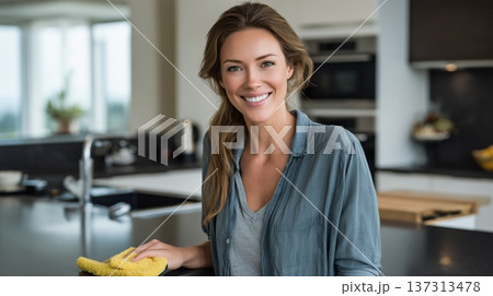 Cheerful Young Woman in Modern Kitchen Holding Cleaning Cloth with Shiny Countertop and Natural Ligh 137313478