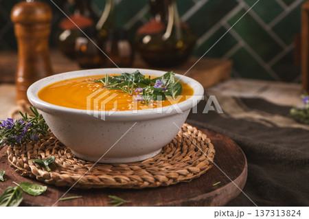 Creamy Pumpkin Soup Garnished with Fresh Herbs and Sesame Seeds in a Rustic Kitchen Setting 137313824