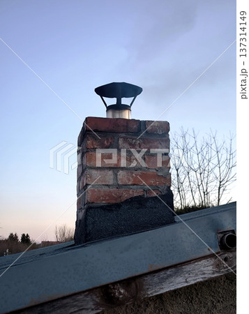 Smoke from a brick chimney against a blue sky, heating a country house or cottage in winter Smoke from a brick chimney against a blue sky, heating a country house or cottage in winter 137314149