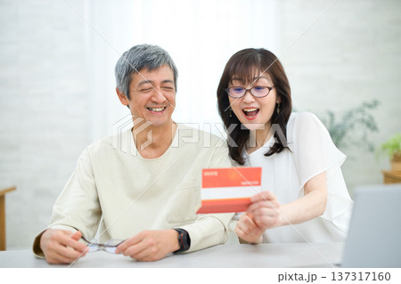 リビングで貯金通帳を見る60代の夫婦 リビングで貯金通帳を見る60代の夫婦 137317160