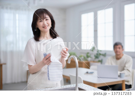 キッチンでお皿を拭きながら笑顔で話す60代女性と男性 137317283