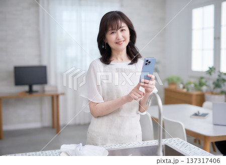 キッチンでスマホを見る60代女性 キッチンでスマホを見る60代女性 137317406
