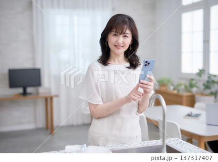 キッチンでスマホを見る60代女性 137317407
