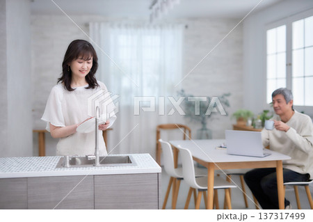 キッチンでお皿を拭きながら笑顔で話す60代女性と男性 キッチンでお皿を拭きながら笑顔で話す60代女性と男性 137317499