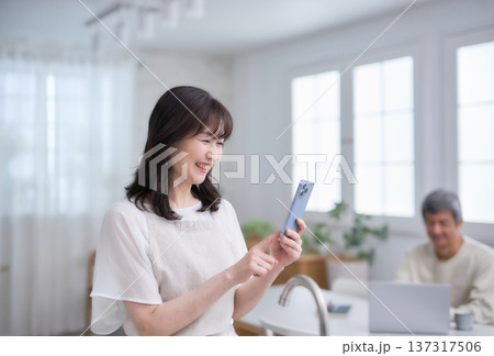 キッチンでスマホを見る60代女性 137317506