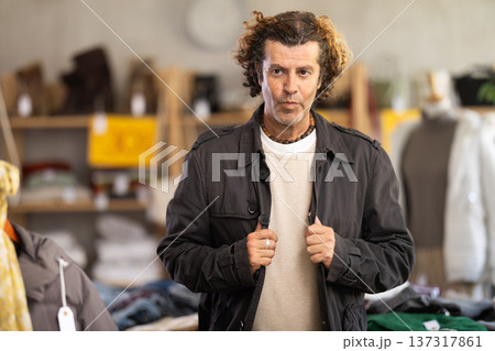 Positive man looking and trying new cloak in clothing shop Positive man looking and trying new cloak in clothing shop 137317861