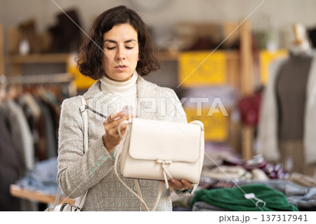 Happy lady customer standing in interior of clothing boutique and choosing fashionable handbag Happy lady customer standing in interior of clothing boutique and choosing fashionable handbag 137317941