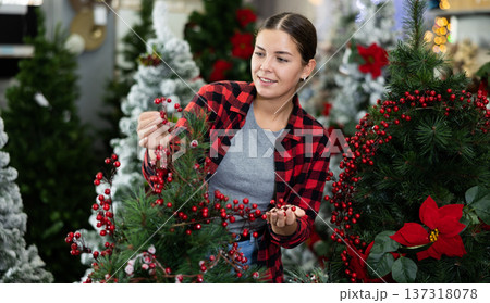 Female seller decorating an artificial Christmas tree with red holly berries at Christmas market 137318078