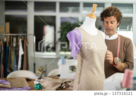 Male tailor standing near mannequin and checking sample quality 137318121