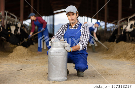 Man farmer standing in cowshed with arms crossed at milk can and smiling Man farmer standing in cowshed with arms crossed at milk can and smiling 137318217