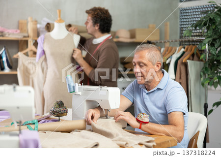 mature woman sews against the background of a tailor and a mannequin mature woman sews against the background of a tailor and a mannequin 137318224