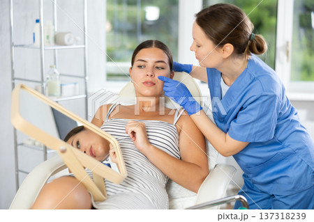 Woman cosmetologist examines patients nasolabial area after lifting procedure and palpates lips mouth Woman cosmetologist examines patients nasolabial area after lifting procedure and palpates lips mouth 137318239
