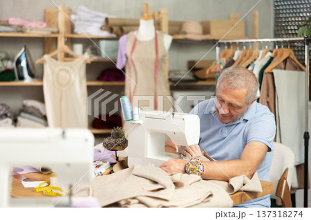 Man tailor sews on sewing machine in workshop Man tailor sews on sewing machine in workshop 137318274