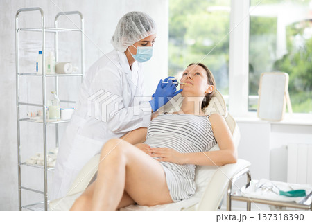Young female cosmetologist makes injection in lips of patient 137318390