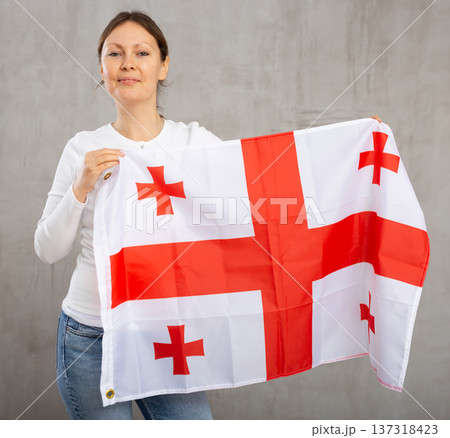 Happy young woman holding flag of Georgia against unicoloured background Happy young woman holding flag of Georgia against unicoloured background 137318423