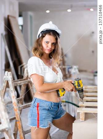Pretty woman in a white blouse and short shorts poses playfully with a screwdriver in renovated room Pretty woman in a white blouse and short shorts poses playfully with a screwdriver in renovated room 137318466