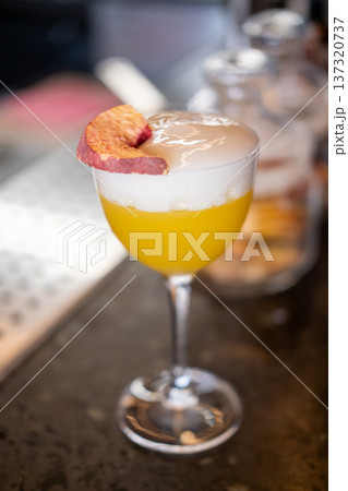 Alcoholic drink. Aperitif glass. Bright yellow tasty juice cocktail with white foam layer garnished with aromatic dried fruit slice. Alcoholic drink. Aperitif glass. Bright yellow tasty juice cocktail with white foam layer garnished with aromatic dried fruit slice. 137320737