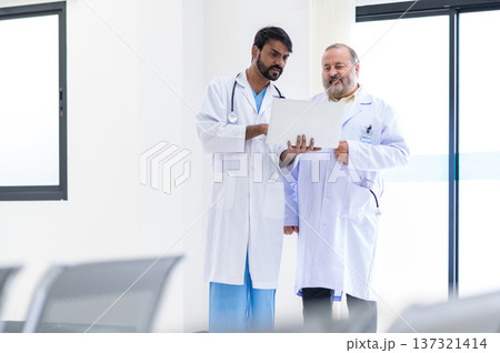 Concentrated mature and young male doctors in white medical uniforms look at laptop computer and discuss patient anamnesis together. team brainstorming make decision concept. 137321414