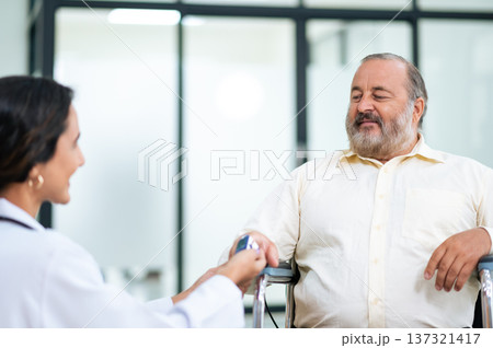 Doctor uses finger pulse oximeter measuring patient man while he sitting in a wheelchair, elderly health checkup, happiness. Doctor uses finger pulse oximeter measuring patient man while he sitting in a wheelchair, elderly health checkup, happiness. 137321417