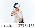 business woman in informal suit wearing VR goggles pointing in the air while standing isolated on white background. concept of Metaverse, virtual reality, future, technology, and internet of things. 137321458