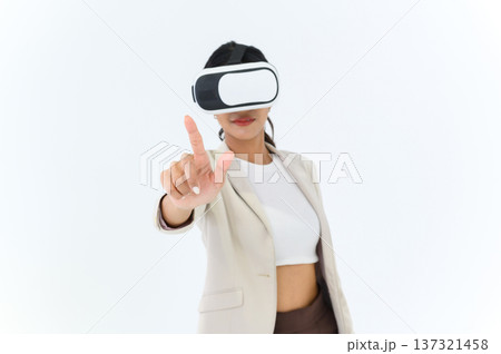 business woman in informal suit wearing VR goggles pointing in the air while standing isolated on white background. concept of Metaverse, virtual reality, future, technology, and internet of things. business woman in informal suit wearing VR goggles pointing in the air while standing isolated on white background. concept of Metaverse, virtual reality, future, technology, and internet of things. 137321458