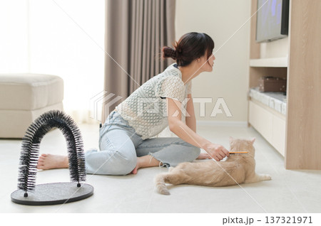 Happy asian woman using brush on friendly pet cat on floor at comfortable home improving mental health and everyday wellness during relaxing indoor activity for animal companion 137321971