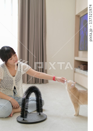Relaxed happy asian woman petting friendly cat pet at home promoting mental health wellness and deep emotional relaxation sitting on floor near scratcher toy Relaxed happy asian woman petting friendly cat pet at home promoting mental health wellness and deep emotional relaxation sitting on floor near scratcher toy 137321974