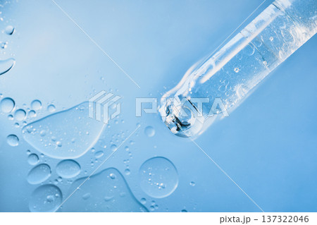 Dropper containing transparent skincare serum with bubbles on light blue liquid surface 137322046
