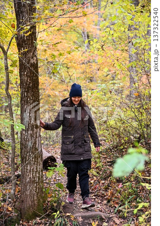 Woman walking along forest trail during autumn solo hike. Calm wellness travel, mindful movement and peaceful rest in nature. 137322540
