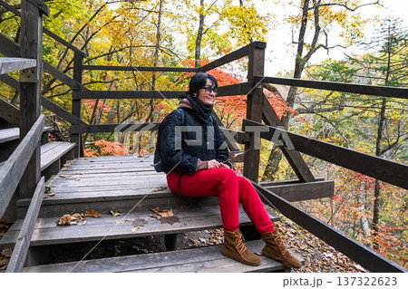 Russian woman 50 years old solo traveler sitting on wooden stairs in autumn forest Russia traveling alone enjoying calm freedom and mindful journey Russian woman 50 years old solo traveler sitting on wooden stairs in autumn forest Russia traveling alone enjoying calm freedom and mindful journey 137322623