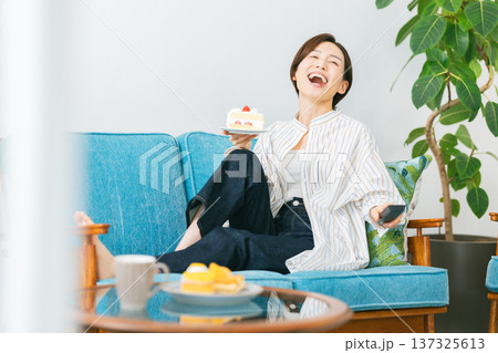 テレビを見ながらソファーでケーキを食べる女性 137325613