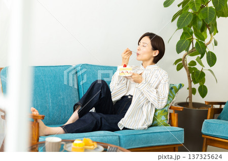 ソファーでくつろぎながらケーキを食べる女性 ソファーでくつろぎながらケーキを食べる女性 137325624